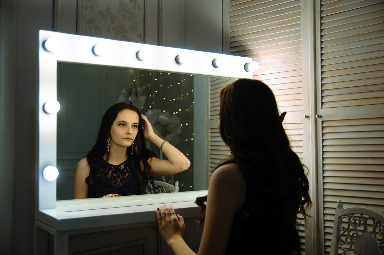 Modelă aranjându-și părul în fața oglinzii luminate, înainte de tură