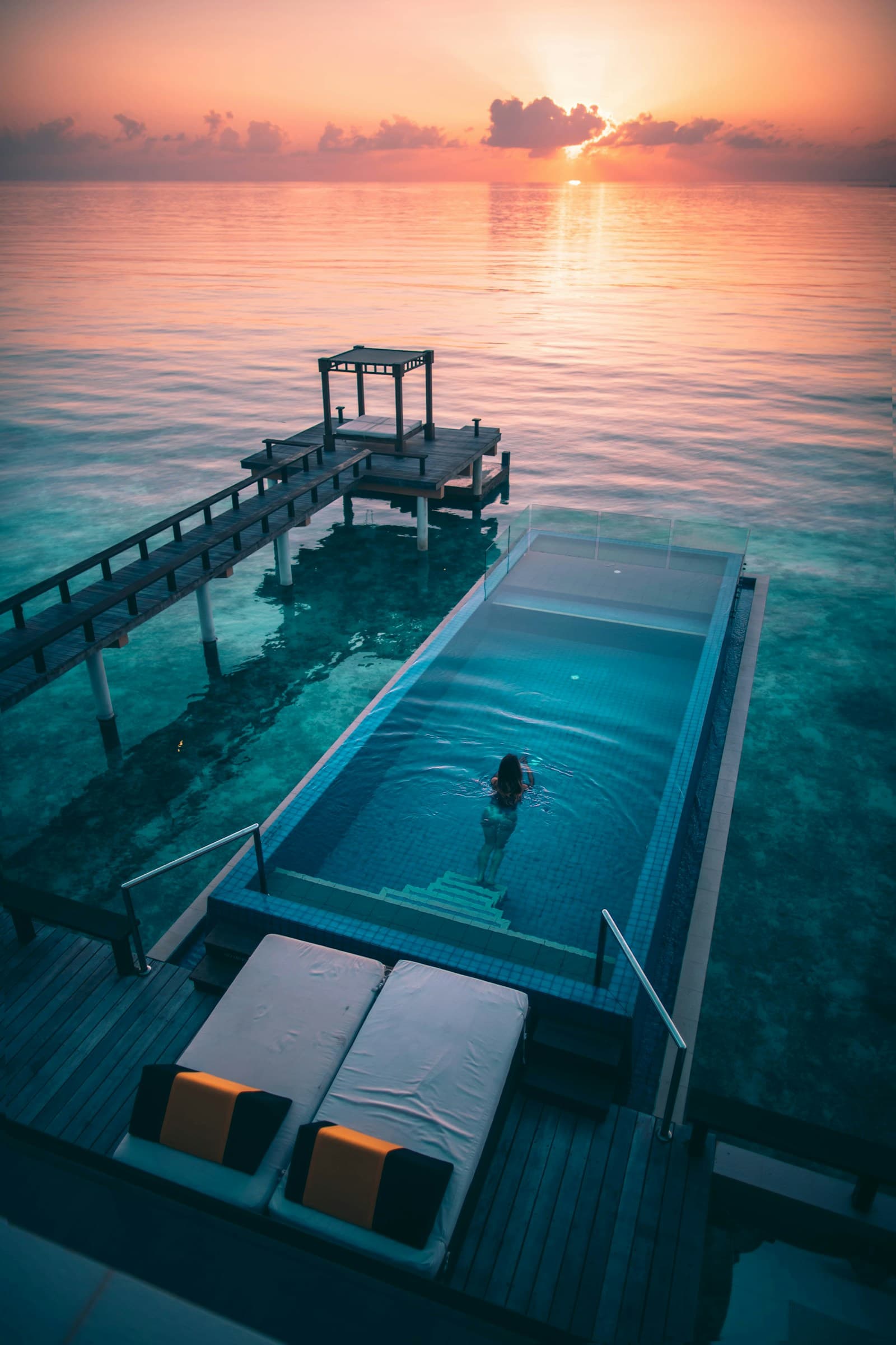 Piscină infinită la răsărit, cu cerul roz reflectat în ocean